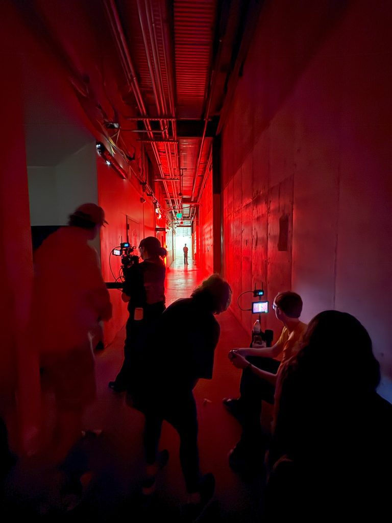 a filmcrew works in a hallway lit with red light